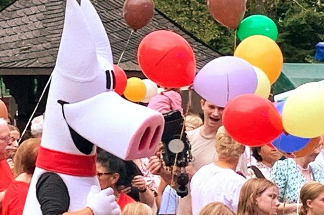 LSB-Maskottchen Schweinehund in einer fröhlichen Menschenmenge umringt von vielen bunten Luftballons